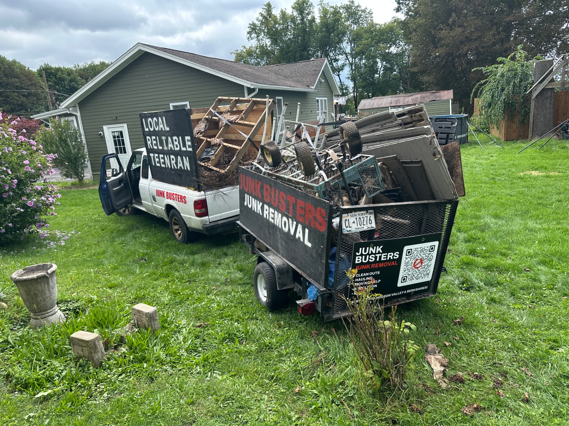Junk Busters truck and trailer loaded to capacity with junk next to a house